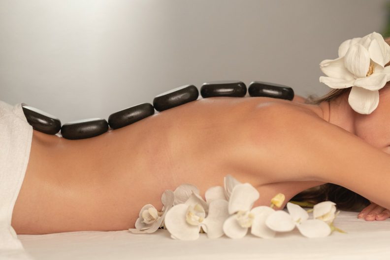 Detailaufnahme einer Frau welche schwarze heiße Steine für eine Massage auf ihrem Rücken liegen hat