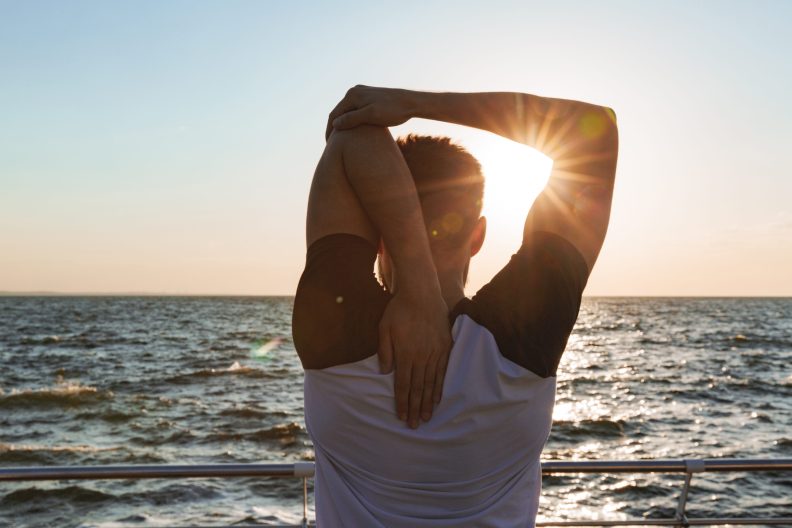 Mann dehnt sich beim Sonnenuntergang am Meer und genießt die Ruhe