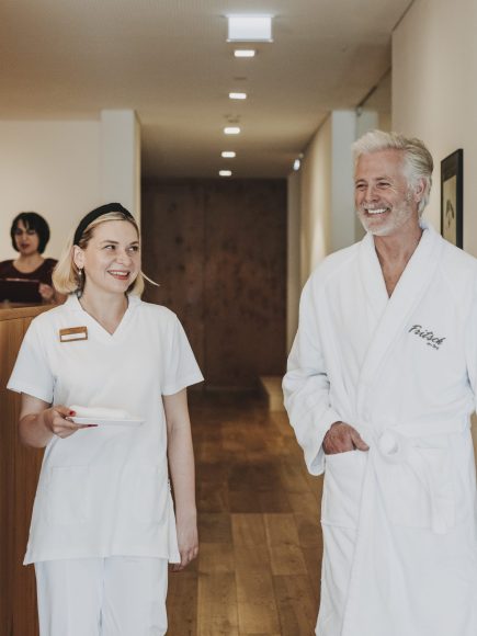 Ein älterer Mann im Bademantel unterhält sich mit einer Mitarbeiterin in einem Wellnesshotel, nachdem er eine Andropause-Behandlung besucht hat