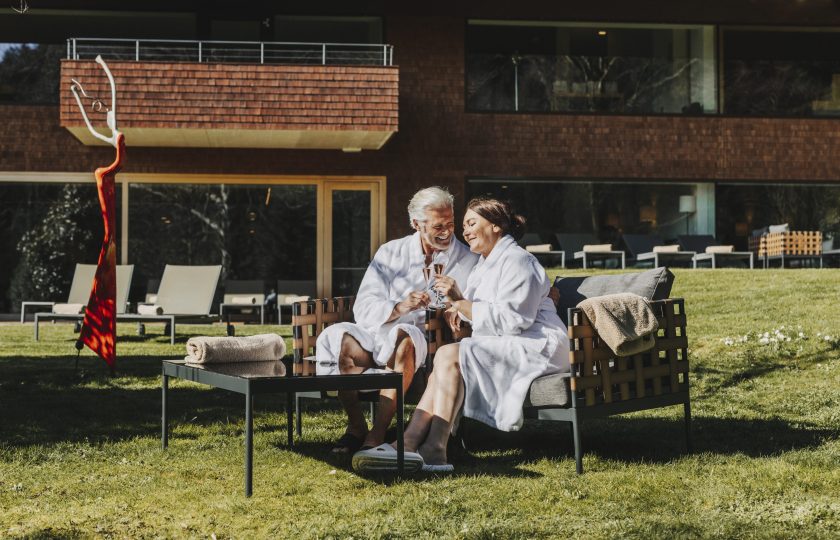 Ein älteres Paar in Bademänteln genießt entspannt ein Glas Sekt im Garten eines Day Spa am Bodensee