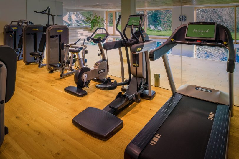 Helle, moderne Fitnessgeräte in einem Raum mit Blick auf den Pool und die grüne Natur in einem Wellnesshotel in Bregenz