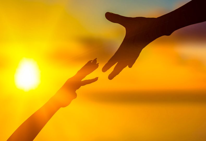 Zwei Hände, die sich im Licht eines leuchtenden Sonnenuntergangs entgegenstrecken, symbolisieren Hoffnung und Unterstützung