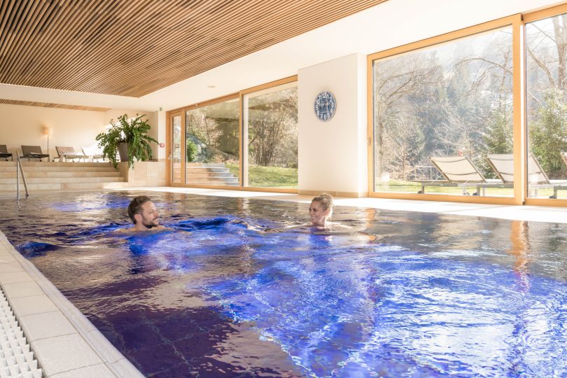 Zwei Personen entspannen im Innenpool eines Wellnesshotels in Bregenz mit Blick auf die Natur