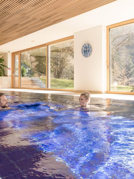 Zwei Personen entspannen im Innenpool eines Wellnesshotels in Bregenz mit Blick auf die Natur