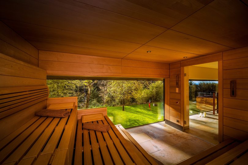 Moderne Sauna in einem Hotel am Bodensee in Österreich mit großem Panoramafenster und Blick auf einen grünen Garten und Bäume