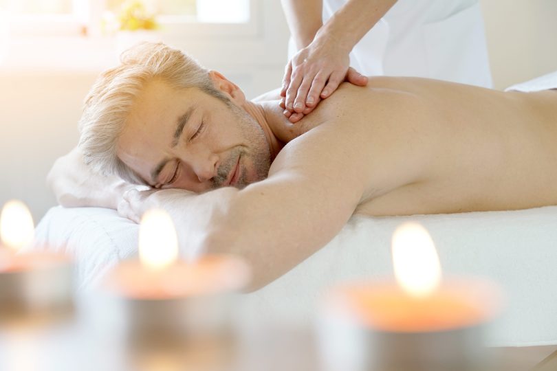 Ein entspannter Mann genießt eine Rückenmassage in einem stimmungsvoll beleuchteten Wellnessraum mit Kerzen