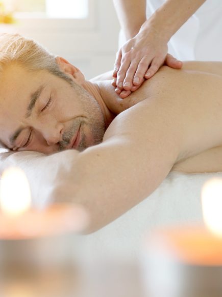 Ein entspannter Mann genießt eine Rückenmassage in einem stimmungsvoll beleuchteten Wellnessraum mit Kerzen