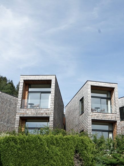 Moderne Chalets mit großen Glasfronten, eingebettet in eine grüne, hügelige Landschaft